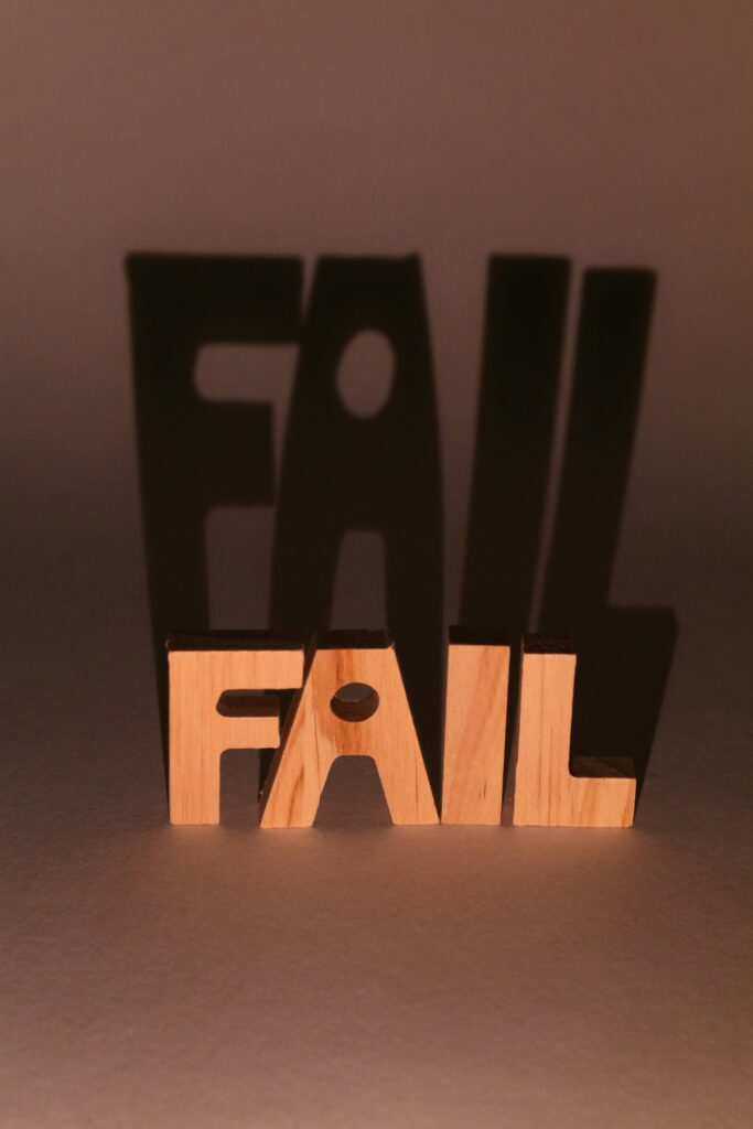 Wooden letters spelling 'FAIL' create dramatic shadows in a studio setting.
