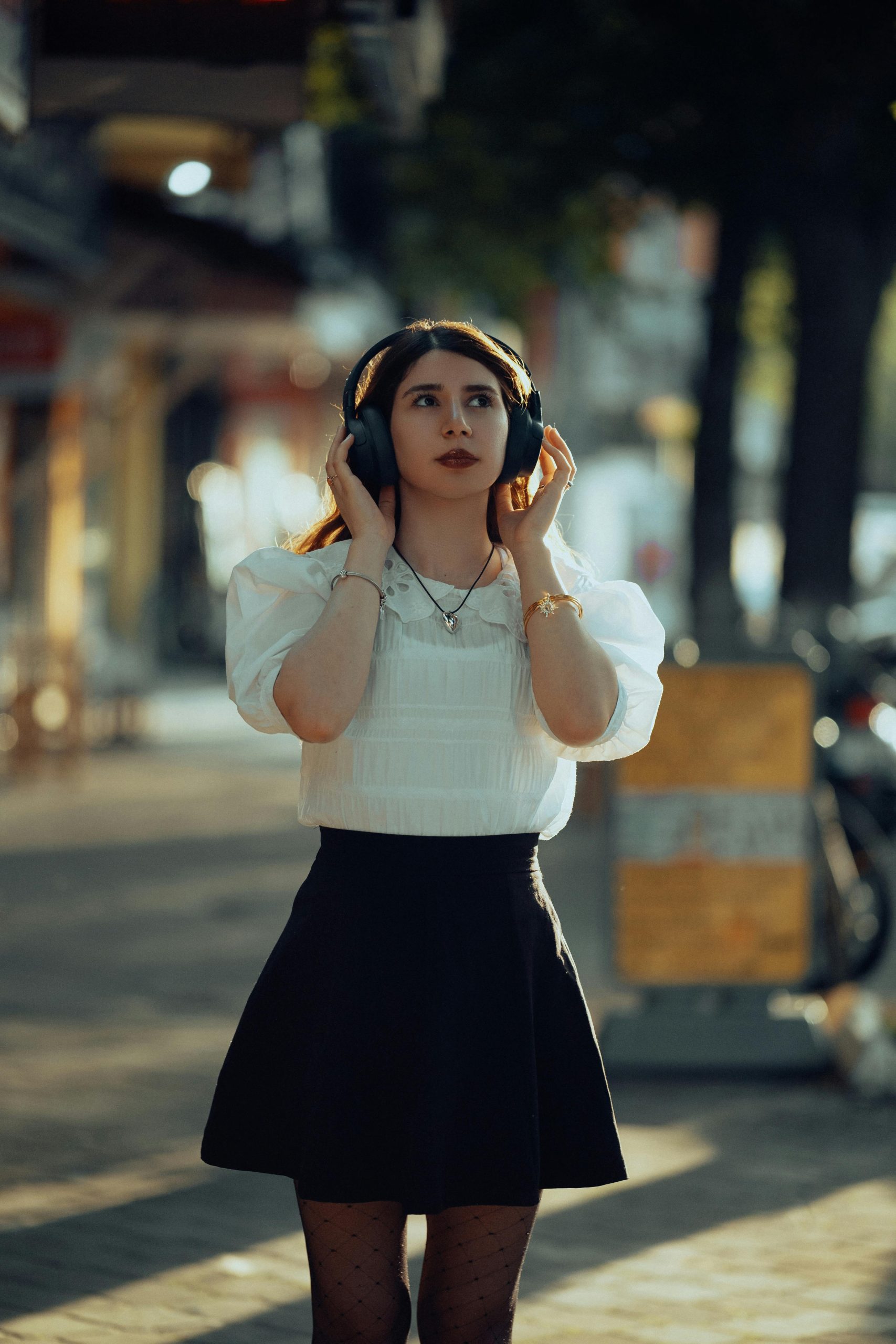 A stylish young woman listens to music with headphones on a sunny fall day outdoors.
