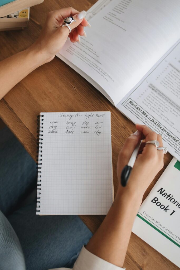 Student taking notes in a notebook surrounded by study materials, textbooks, and worksheets.